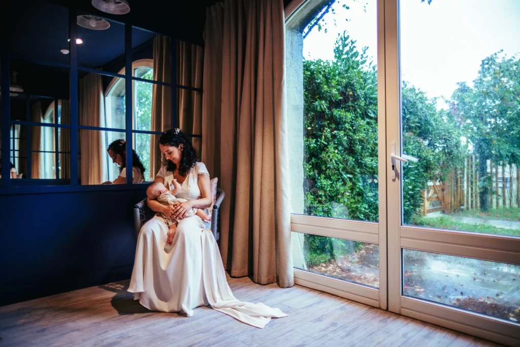 Photo d'une femme en robe de mariée en train d'allaiter son bébé pendant son mariage